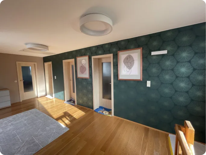 Flur mit Holzboden, drei Holztüren und grüner Wand mit Pflanzenmuster und zwei Bilderrahmen.