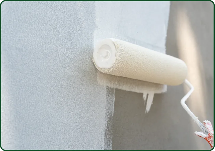 Farbrolle trägt weiße Farbe auf graue Wand beim Streichen auf.